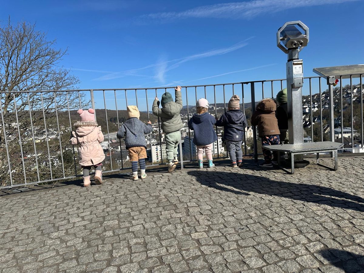 Die Kinder stehen am Geländer eines Aussichtspunkts und schauen über Siegen